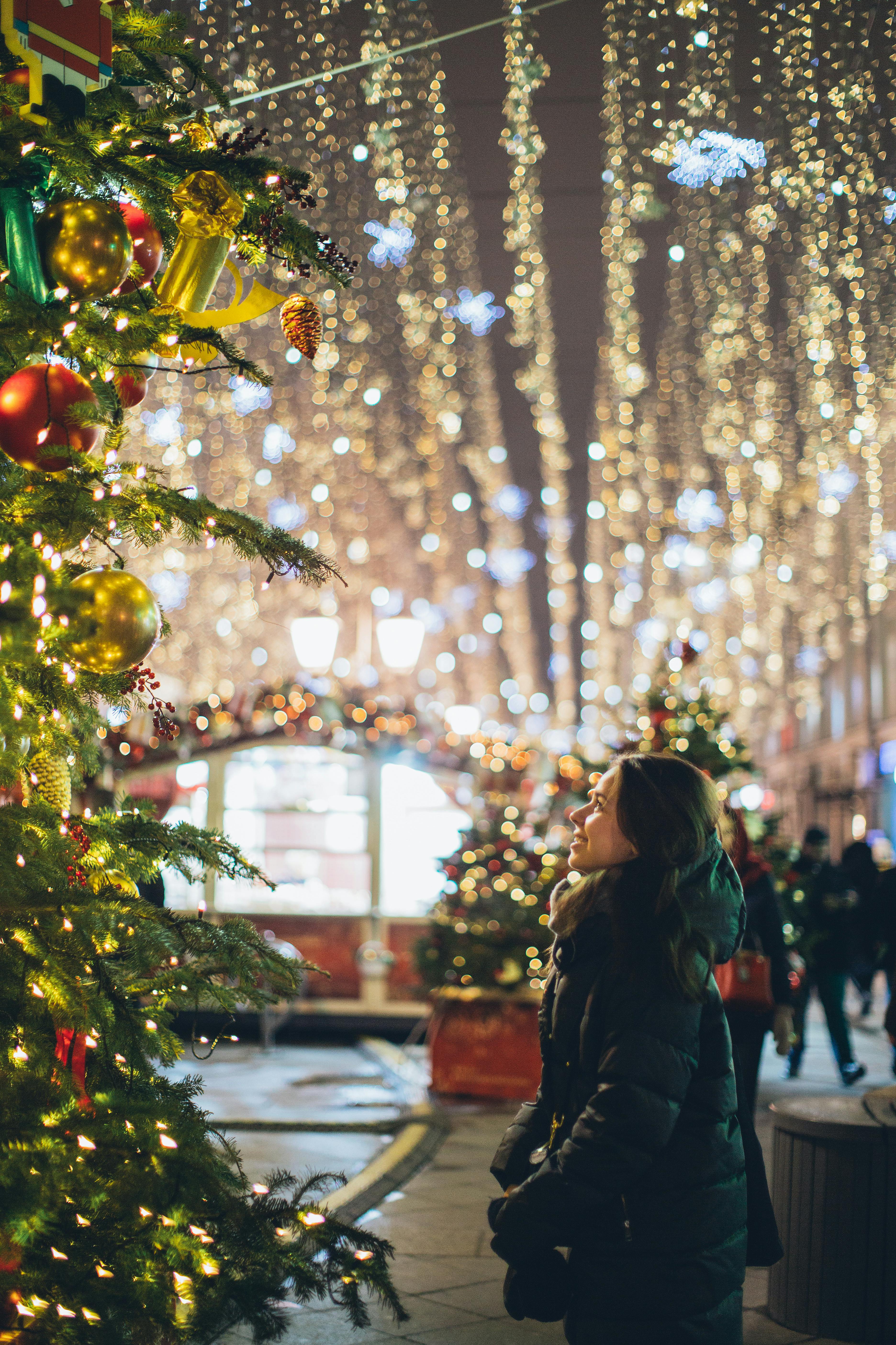 A women stood looking at a big Christmas tree in public with decorations around her