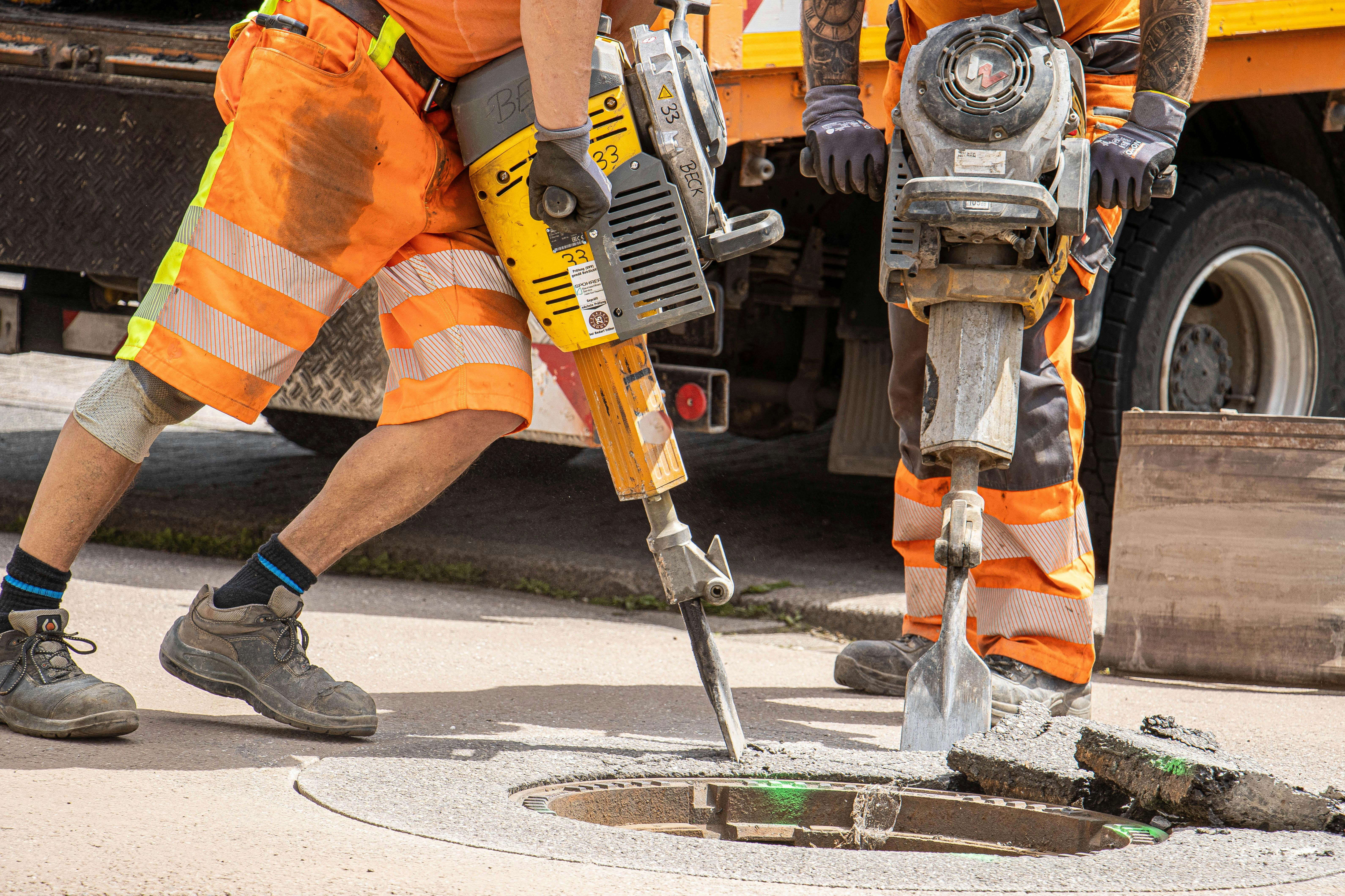 Two men wearing high visibility suits using breakers to drill through concrete ground